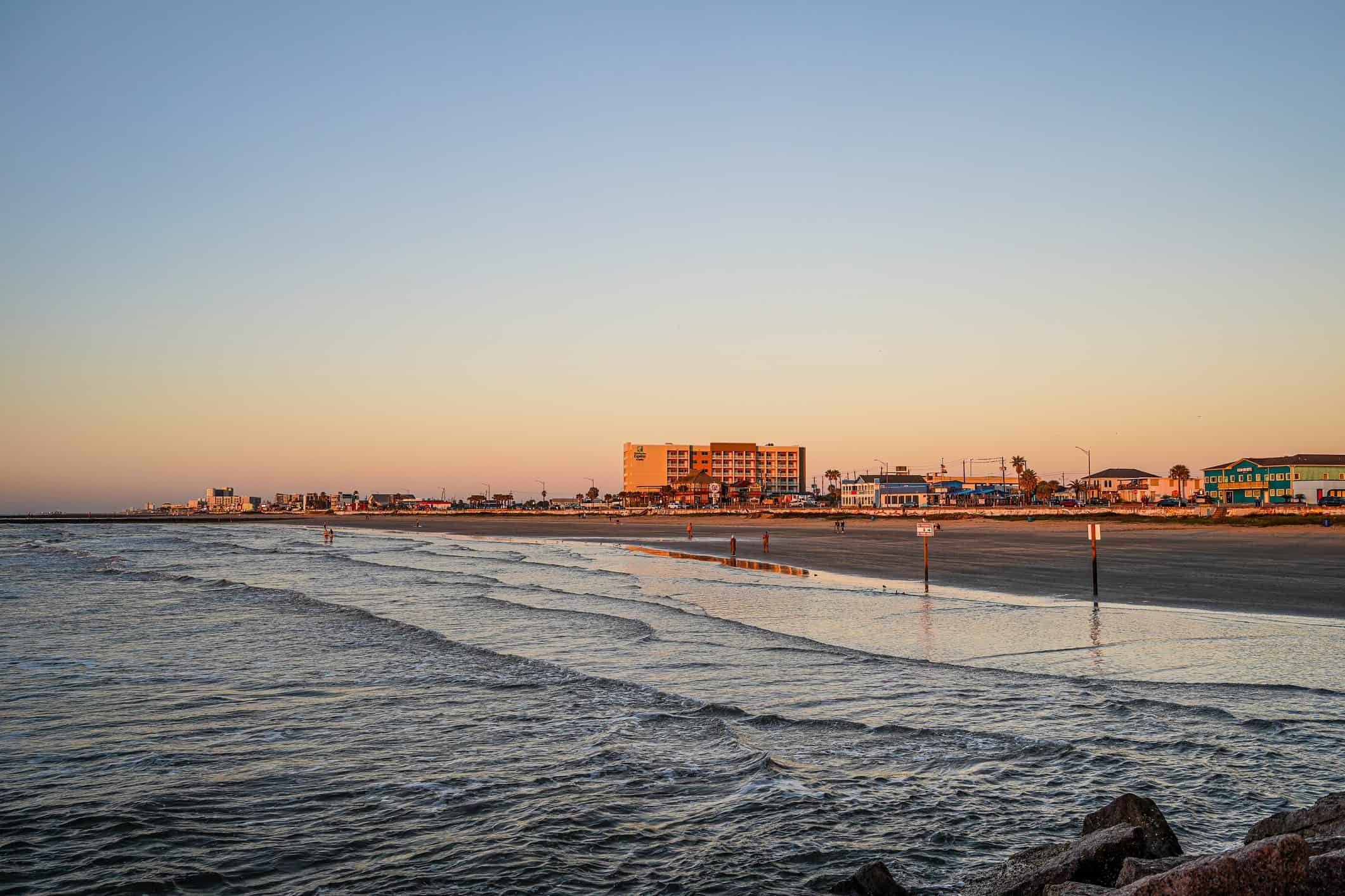People enjoy the beach at sunrise. Hotels and restaurants on the Strand by the Gulf of Mexico, Galveston, Texas, USA